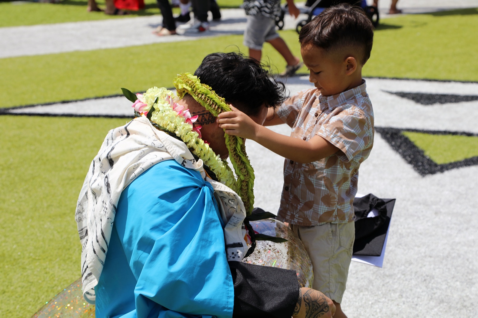 A child placing a maile lei on Tre Zamora at a ceremony