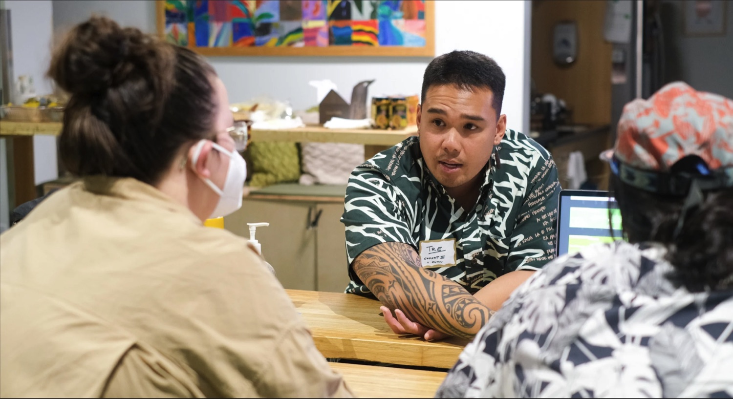 Tre Zamora in a green aloha shirt talking with collaborators across a table during a work session