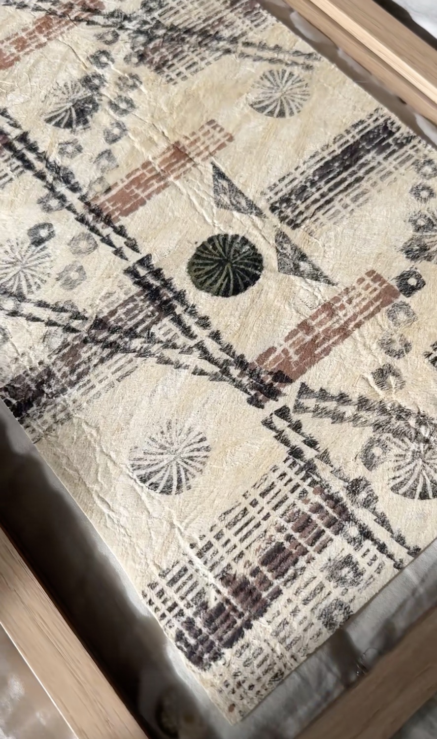 Hand-decorated Hawaiian kapa (bark cloth) with geometric patterns, resting in a wooden tray